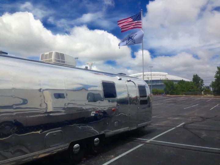 An Airstream RV rental gleaming in a stadium parking lot, with US & Dallas Cowboys flags flying.. Airstream Sovereign 1973