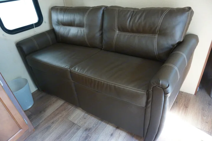 Modern brown sofa with white stitching in an RV rental interior, showing window and wood-look flooring.. Dutchmen Aspen Trail 2015