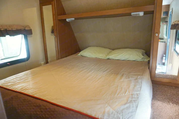 RV rental bedroom: A cozy, compact space with a comfortable bed, window, and mirrored wardrobe.. Dutchmen Aspen Trail 2015