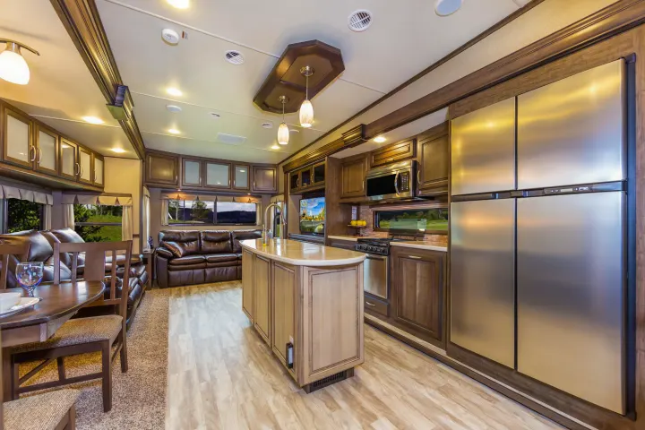 Inside a modern RV rental: open-plan living room with brown sofas, dining area, and a fully equipped kitchen.. Grand Design Solitude 2016