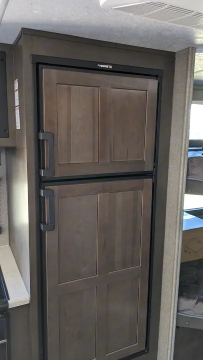 This RV rental features a built-in Dometic refrigerator/freezer with stylish dark wood-paneled doors and black handles.. Forest River Rockwood Mini Lite 2020