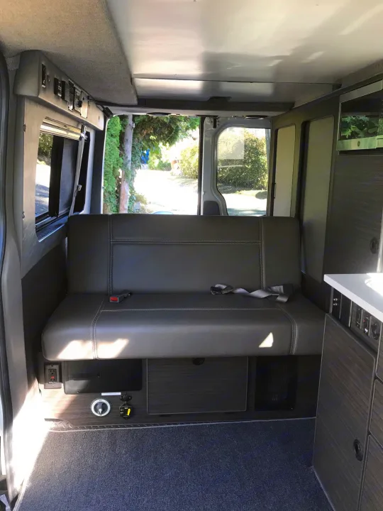 RV rental interior: a comfy gray bench seat, kitchenette, and accessible controls, ideal for your next adventure.. Mercedes Sprinter 2018