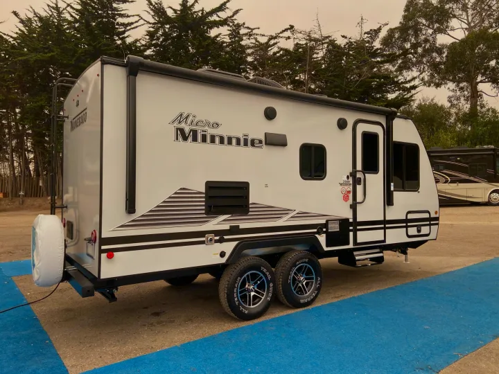 A white Winnebago Micro Minnie travel trailer, ideal for an RV rental, is parked outdoors, ready for adventure and camping.. Winnebago Micro Minnie 2021