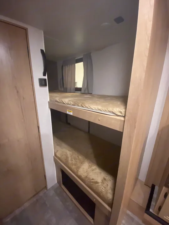 This RV rental interior features sturdy wooden bunk beds with comfortable tan mattresses, providing a compact sleeping area.. Winnebago Micro Minnie 2021