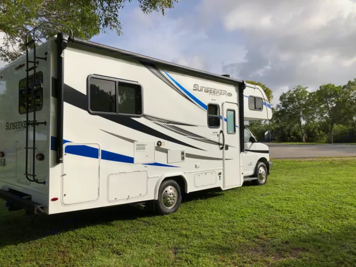 A white Sunseeker RV rental with blue and black stripes is parked on green grass. Perfect for your next adventure.. Forest River sunseeker LE 2350 2020