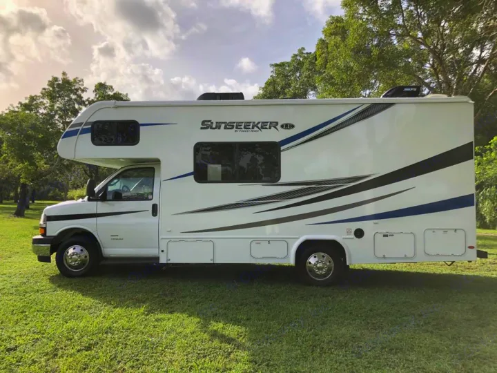 This white Sunseeker RV rental, featuring blue and grey graphics, is parked on lush green grass for your next adventure.. Forest River sunseeker LE 2350 2020