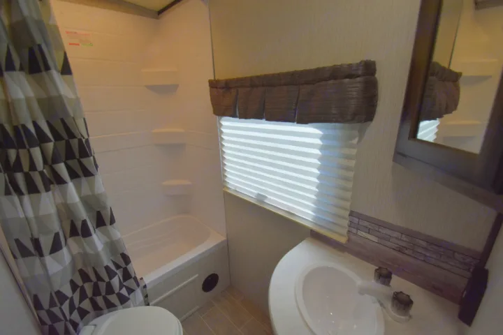Inside an RV rental: a compact bathroom with patterned shower curtain, small tub, window, and sink.. Other Other 2020