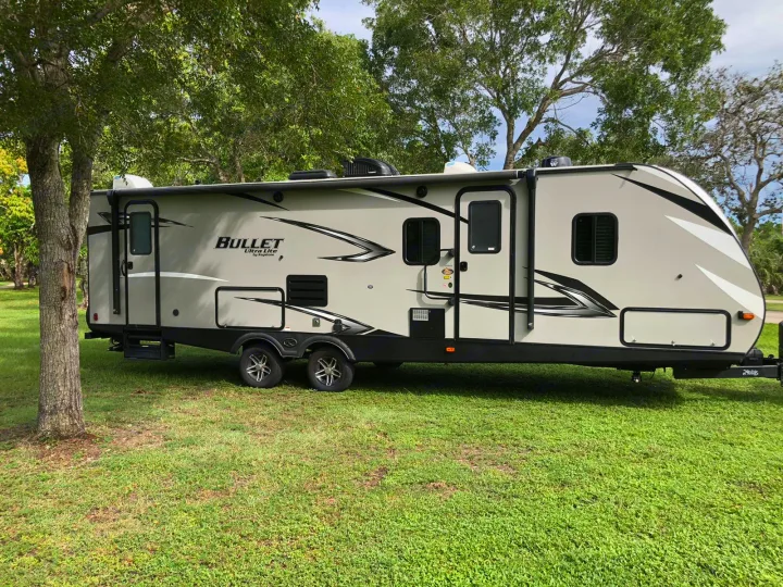 Large, light gray Bullet Ultra Lite travel trailer parked on green grass. Your next RV rental for camping adventures!. Keystone Bullet 2020