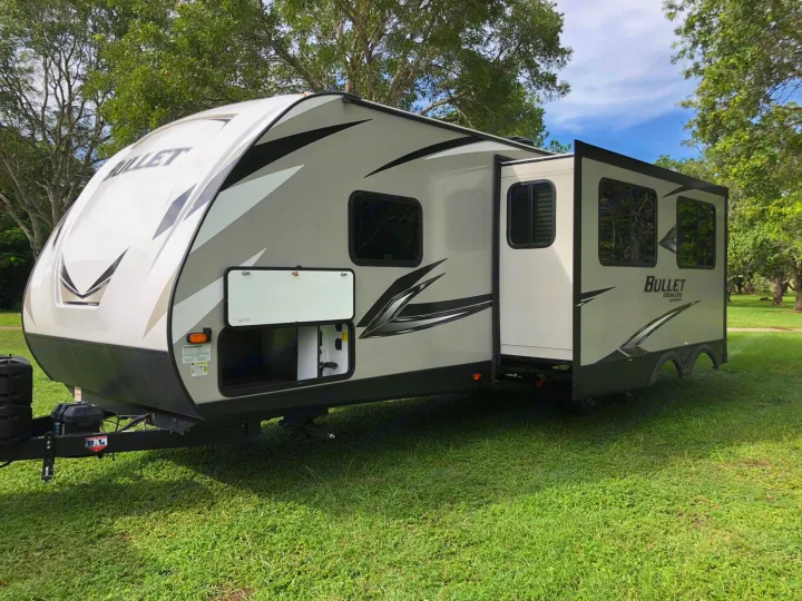 Explore the outdoors with this Bullet travel trailer RV rental, featuring a spacious slide-out, parked on green grass.. Keystone Bullet 2020