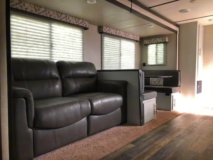 Spacious RV rental living area: gray sofa on carpet, dinette with wood floor, and bright windows.. Keystone Bullet 2020