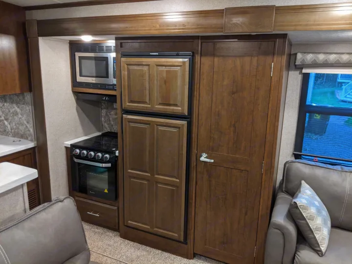 Detailed view of an RV rental's kitchen, showcasing a microwave, Dometic fridge, and stove, adjacent to the living room sofa.. Forest River Forest River Flagstaff Classic Super Lite 2021