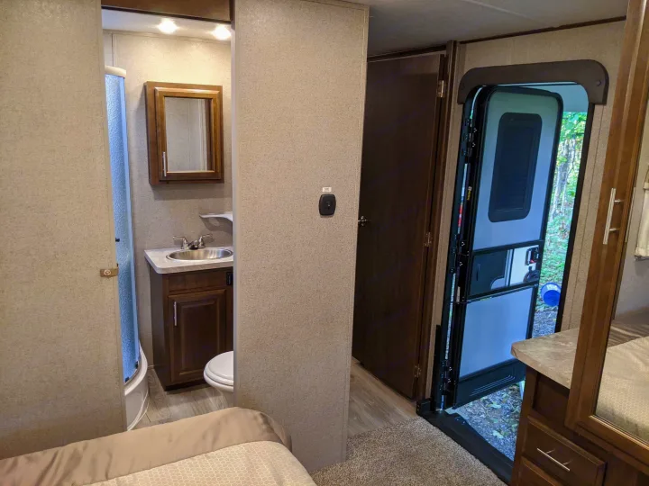 Inside this RV rental: view of the compact bathroom (shower, sink, toilet) and main door open to nature.. Forest River Forest River Flagstaff Classic Super Lite 2021