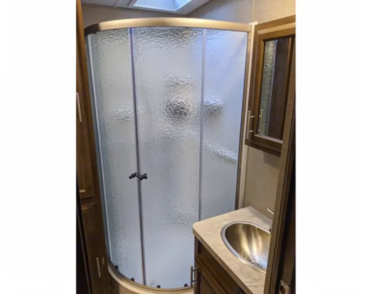 RV rental bathroom featuring a curved, frosted glass shower, compact vanity with a stainless steel sink, and storage cabinet.. Forest River Forest River Flagstaff Classic Super Lite 2021