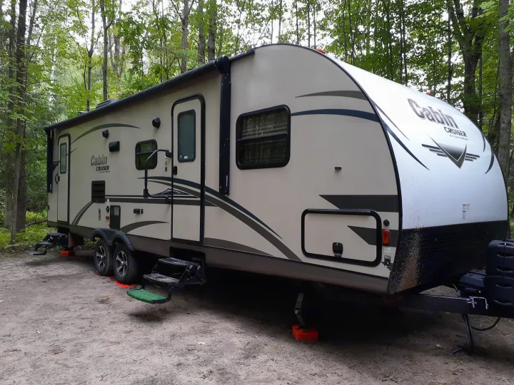 This RV rental, a Cabin Cruiser travel trailer, is parked on a dirt campsite surrounded by green trees, ready for camping.. Gulfstream Cabin Cruiser 2018