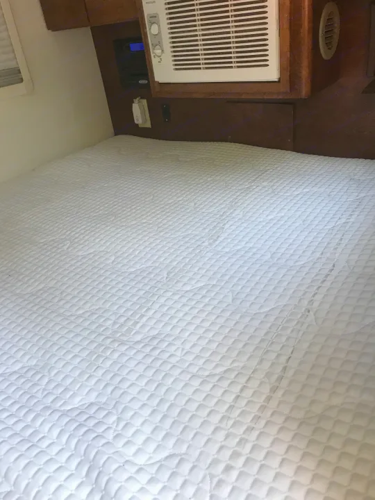 Clean white quilted bed in an RV rental bedroom, featuring an AC unit and control panel mounted above the bed.. T@G T@G Trailer 2015