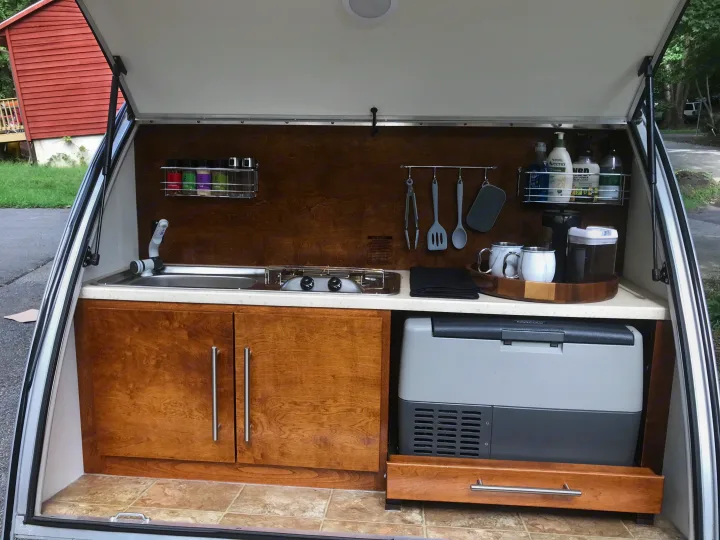 Compact outdoor kitchen in an RV rental, featuring sink, stove, fridge, and storage, perfect for camping.. T@G T@G Trailer 2015