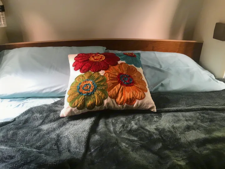 Comfort in an RV rental: light blue bedding, plush gray blanket, & a vibrant floral pillow on the bed.. T@G T@G Trailer 2015