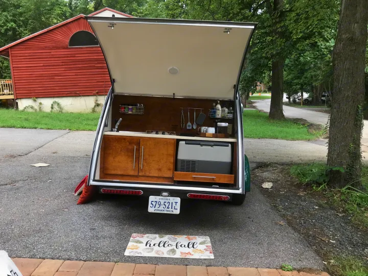 This RV rental shows its open rear kitchen in a teardrop trailer, featuring a sink, fridge, and cabinets.. T@G T@G Trailer 2015