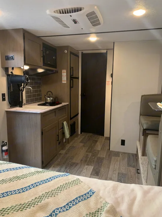 Modern RV rental interior with a compact kitchenette, dinette, and comfortable bed visible, perfect for travel.. Keystone Hideout 2021