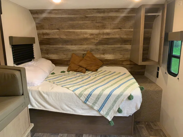 Inside your RV rental: a compact and cozy bedroom with a comfortable bed, rustic wood walls, and clever storage solutions.. Keystone Hideout 2021