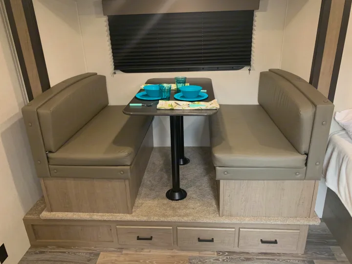 RV rental dinette with cozy booth seating, table set with blue dishes, and accessible storage drawers.. Keystone Hideout 2021