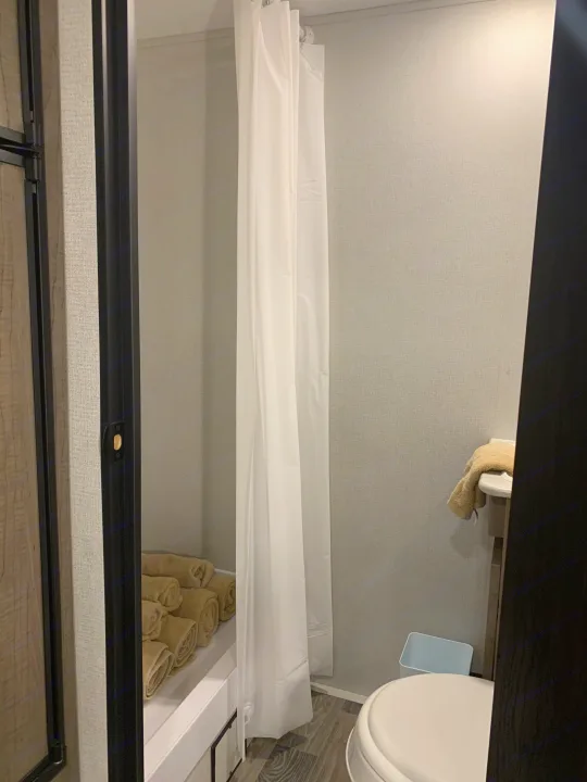 Inside an RV rental: a compact bathroom featuring a shower with curtain, toilet, and fresh towels.. Keystone Hideout 2021