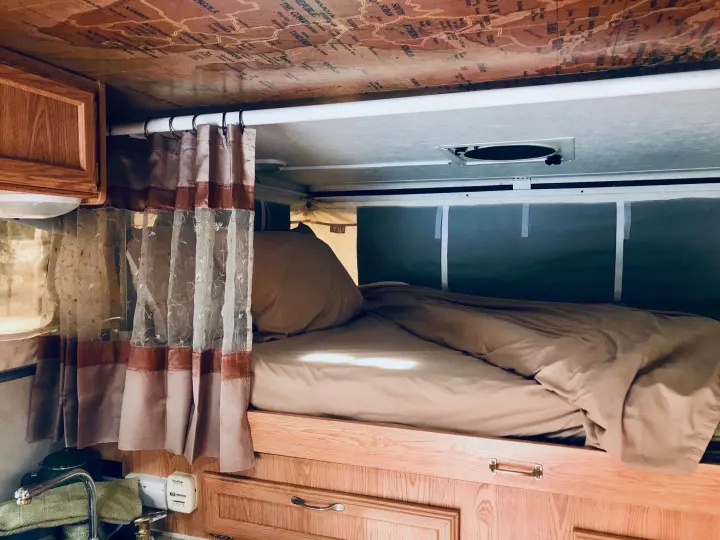 Cozy RV rental interior with a comfy bed, functional sink area, and unique map-patterned ceiling.. Ford F250 2005