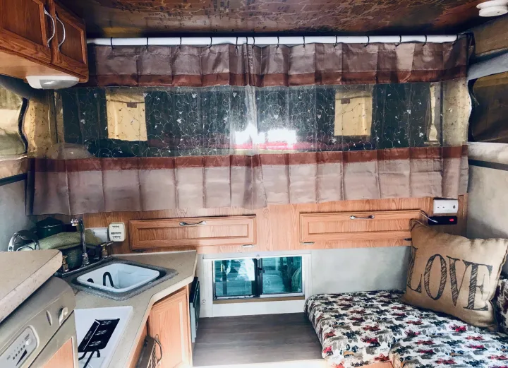 Inside an RV rental, a functional kitchen with a sink, a cozy bed, and privacy curtains create a welcoming space.. Ford F250 2005