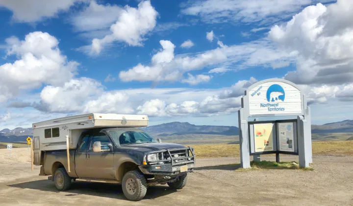 A rugged truck camper at the NWT border sign, mountains under blue sky. Perfect for an outdoor RV rental road trip.. Ford F250 2005