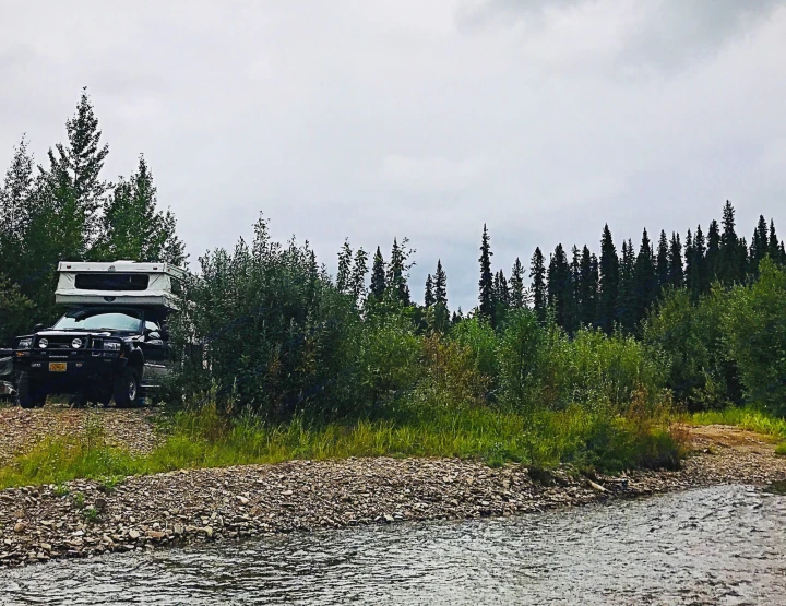 Overcast day camping in an RV rental truck camper by a tranquil forest river.. Ford F250 2005