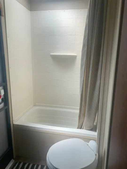 Clean RV rental bathroom featuring a white shower/tub combo, a striped curtain, and a toilet in the foreground.. Dutchmen Aspen Trail 2014