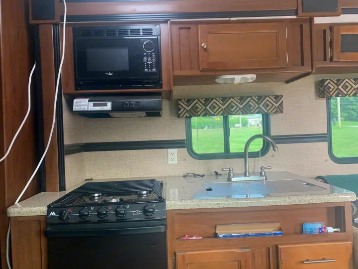 RV rental kitchen: Features a microwave, gas range, sink with faucet, and cabinets. Large windows offer outdoor views.. Dutchmen Aspen Trail 2014