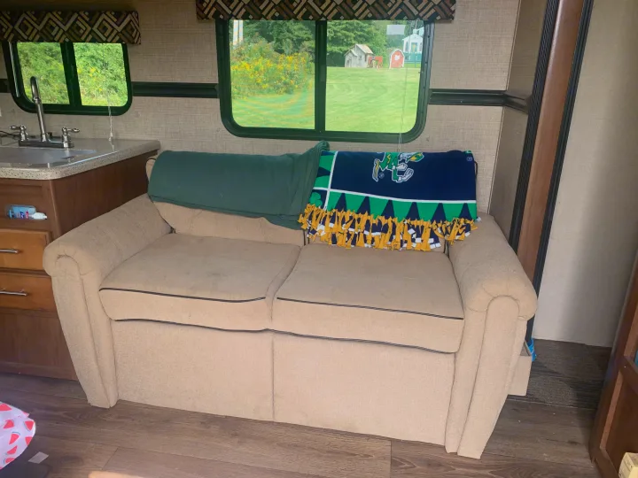 RV rental living area with a sofa, kitchen, and a window view of small outdoor structures and greenery.. Dutchmen Aspen Trail 2014