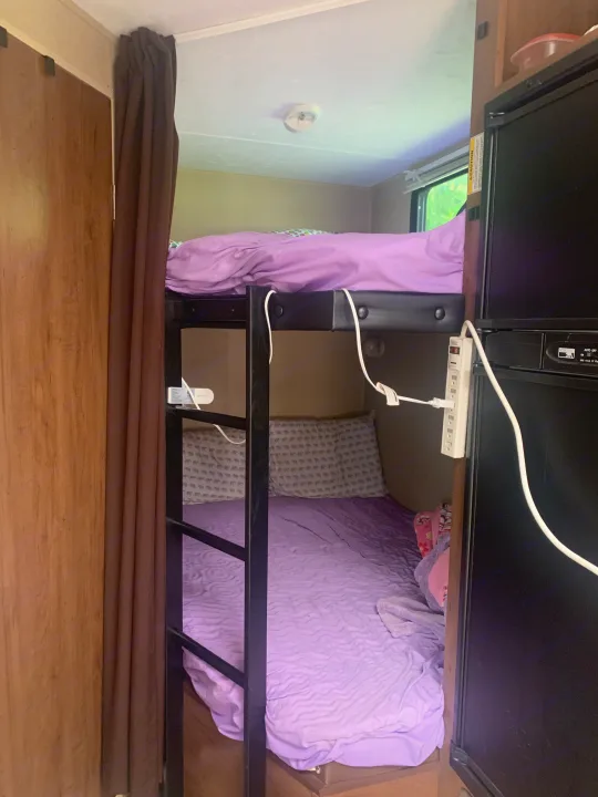An RV rental's sleeping area: two bunk beds with purple sheets, a power strip, fridge, and brown privacy curtain.. Dutchmen Aspen Trail 2014
