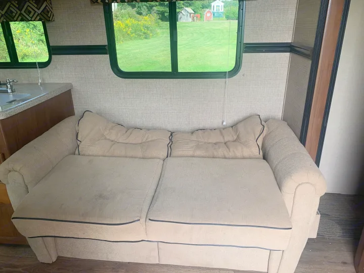 RV rental interior featuring a cozy pull-out sofa, small kitchen area, and a lush green outdoor view from the windows.. Dutchmen Aspen Trail 2014