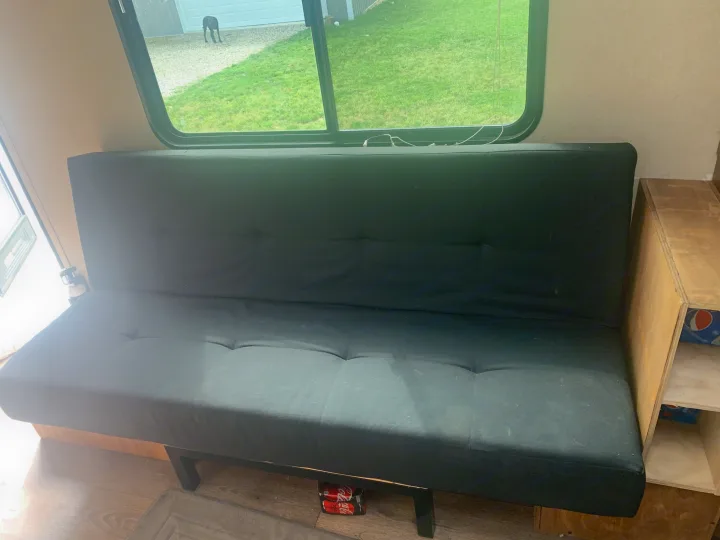 RV rental interior with a black futon, window view of a yard and dog, plus built-in wooden storage.. Dutchmen Aspen Trail 2014