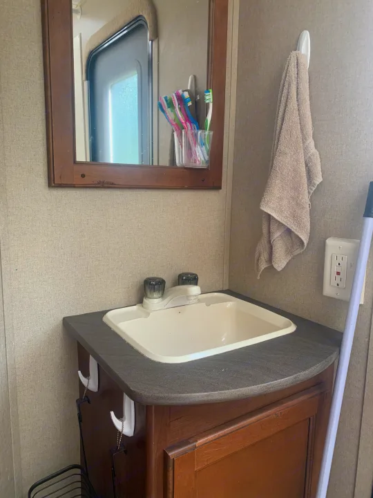 Compact RV rental bathroom: Sink, mirror, toothbrushes, towel, and outlet in a small, functional space.. Dutchmen Aspen Trail 2014