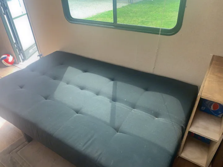 Cozy RV rental interior featuring a dark futon, window with a green view, and wooden storage for a comfortable stay.. Dutchmen Aspen Trail 2014