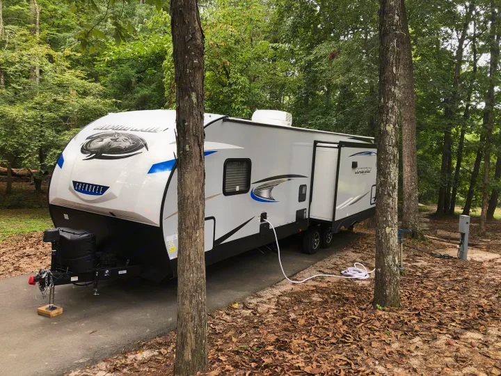 This Alpha Wolf travel trailer, ideal for an rv rental, is parked amidst trees at a serene campsite with visible utility hookups.. Forest River Cherokee Alpha Wolf 2021