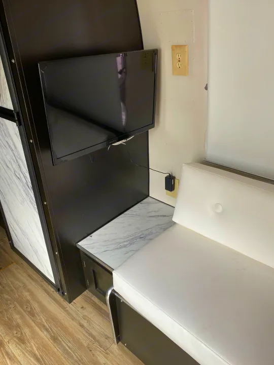 Inside an RV rental: Compact living space with wall-mounted TV, white sofa, and marble counter.. Airstream Sovereign 1973