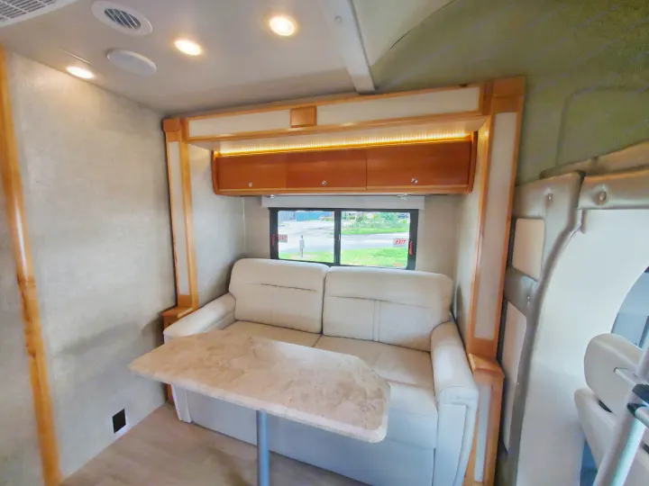 Comfortable RV rental living area with light sofa, dining table, overhead cabinets, and warm accent lighting.. Wayfarer Wayfarer Motorhome 2017