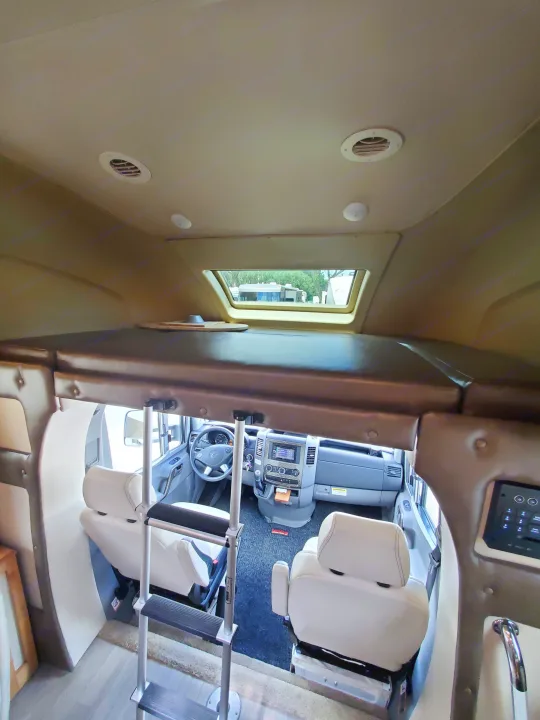Inside an RV rental: View from the living area towards the driver's cab, showing an overhead bed with ladder and dashboard.. Wayfarer Wayfarer Motorhome 2017