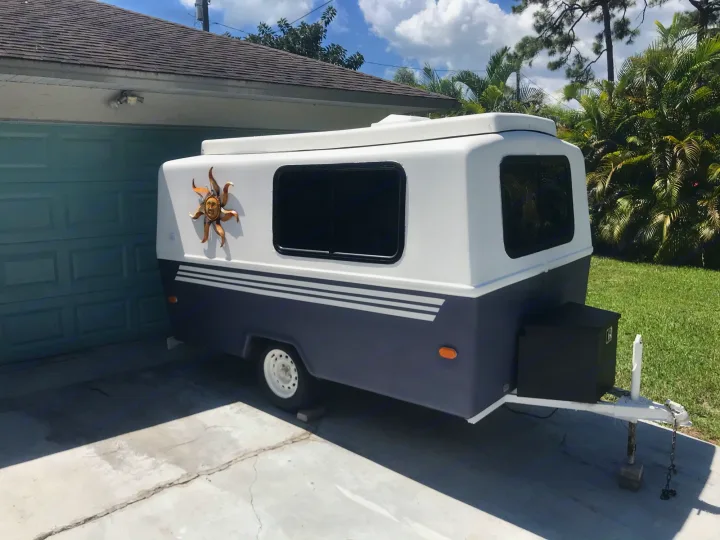 A small white and dark gray travel trailer, featuring sun decor, parked in a driveway. Great for an RV rental adventure!. Hunter Compact Junior 1971