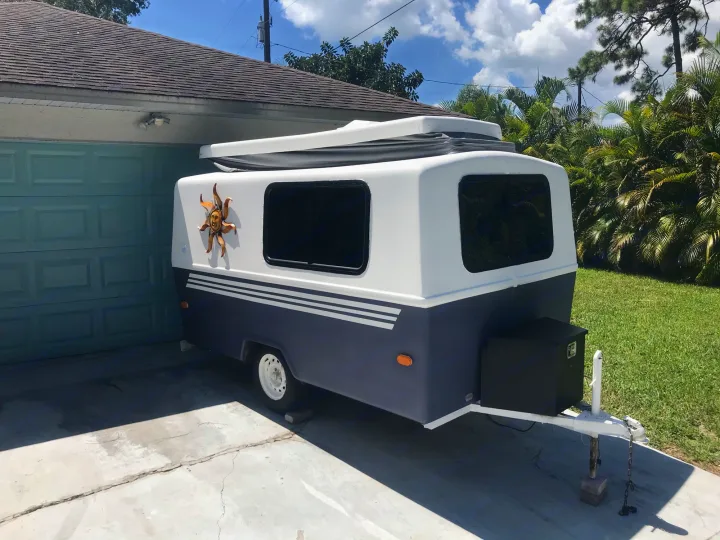 Enjoy this charming compact rv rental, a two-toned camper with a sun decal, ready for adventure parked in a sunny driveway.. Hunter Compact Junior 1971