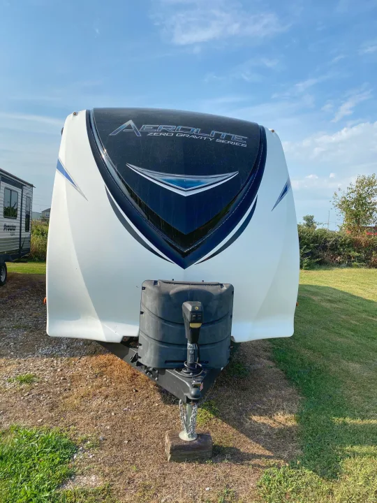 Front view of a white Aerolite travel trailer RV rental, with black accents and a hitch, parked outdoors on dry grass.. Dutchmen Aerolite 2017