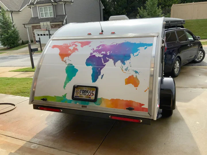 Back of a white RV rental teardrop trailer with a vivid world map design, parked on a driveway.. nuCamp T@G 2019