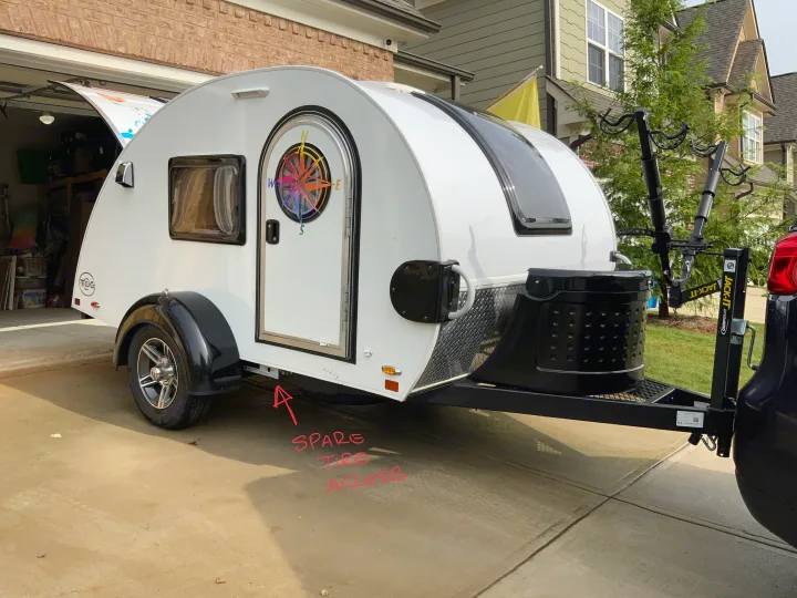 A white T@G teardrop camper, ideal for RV rental, featuring a front bike rack & a colorful compass door design.. nuCamp T@G 2019