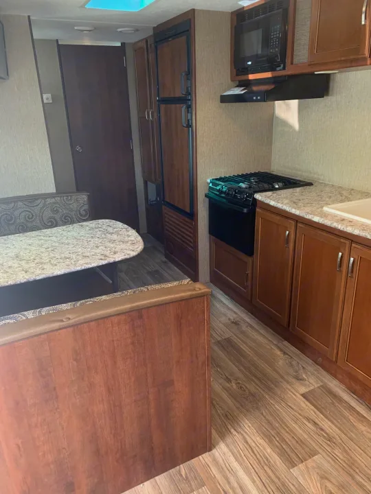 Bright RV rental interior featuring a well-equipped kitchen with a stove, microwave, fridge, and a comfy dinette area.. Keystone Passport 2017