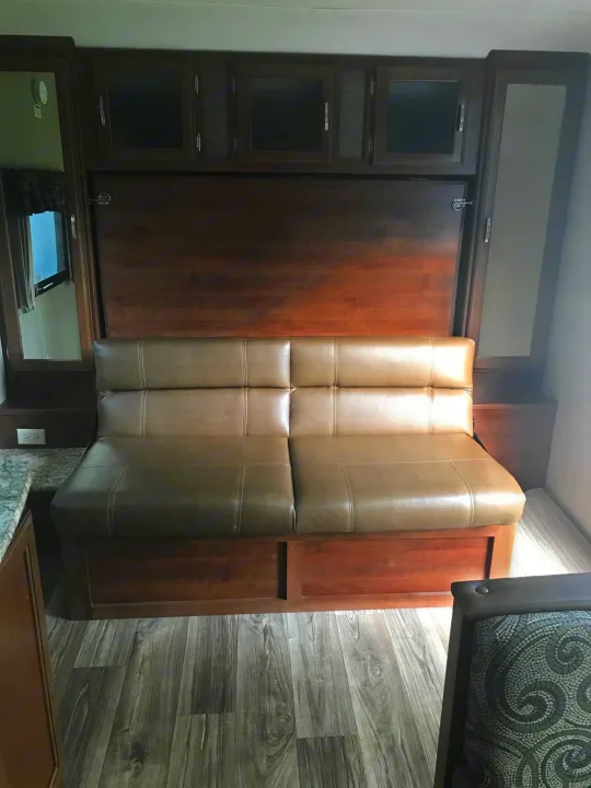 RV rental's versatile interior: a comfy brown sofa, ready to convert to a bed, with overhead cabinets and mirrored storage.. Keystone Passport 2017
