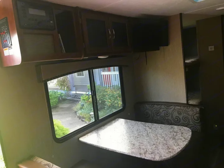 RV rental interior: a comfy dinette with patterned seats, speckled table, large window, plus entertainment center & controls.. Keystone Passport 2017
